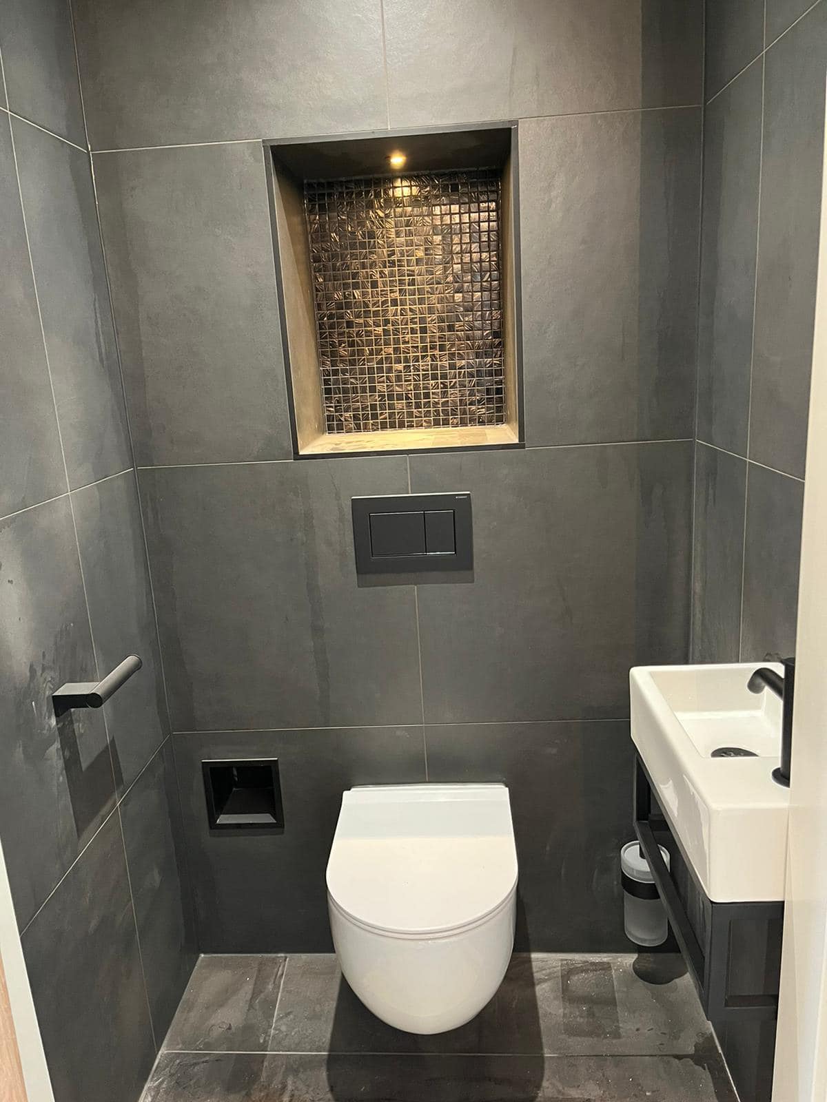 Toiletruimte: Donkere tegels, een verlichte nis met mozaïek en een fonteintje.