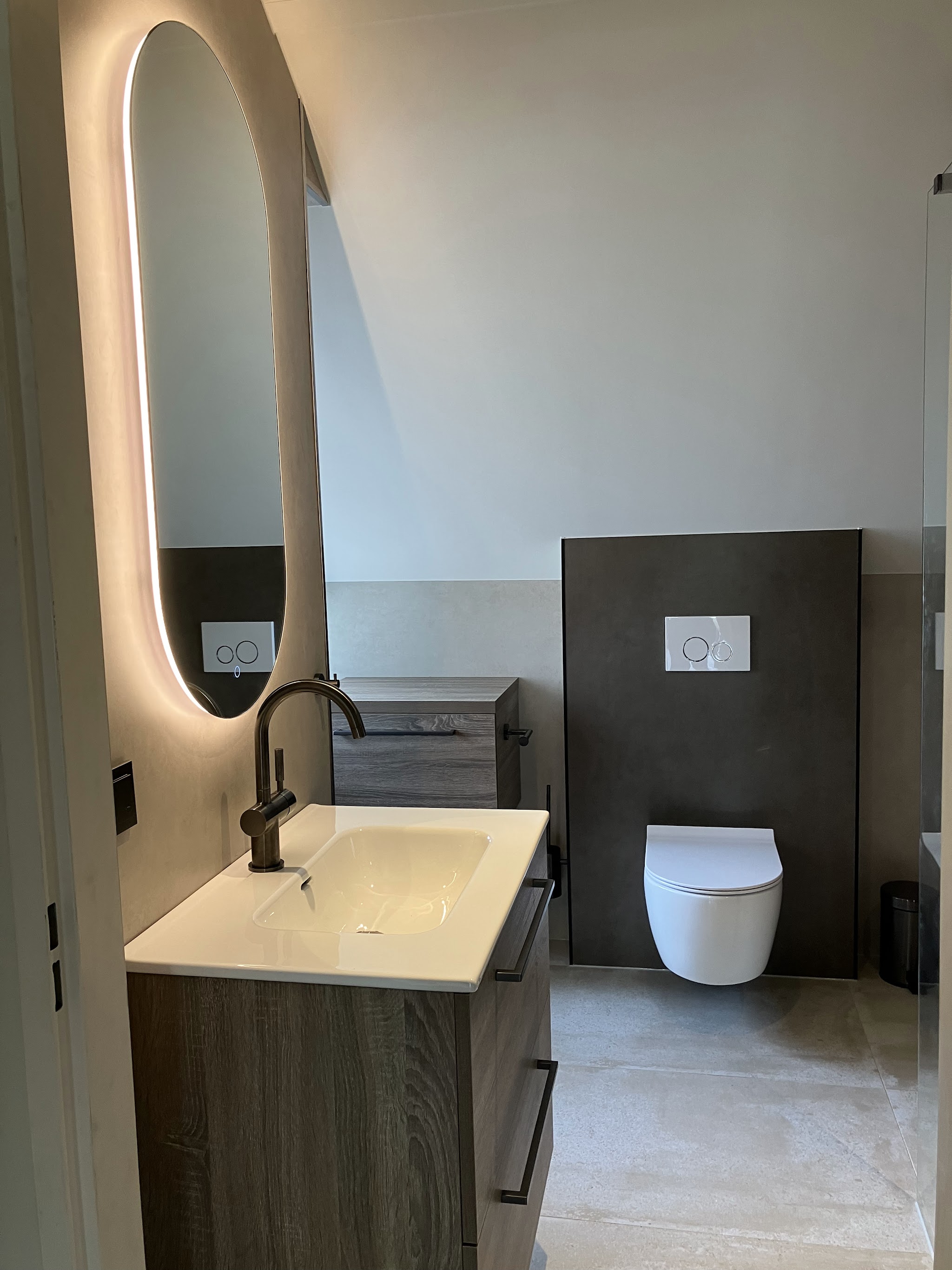 Lichte badkamer: Badmeubel van hout met een verlichte ovale spiegel.