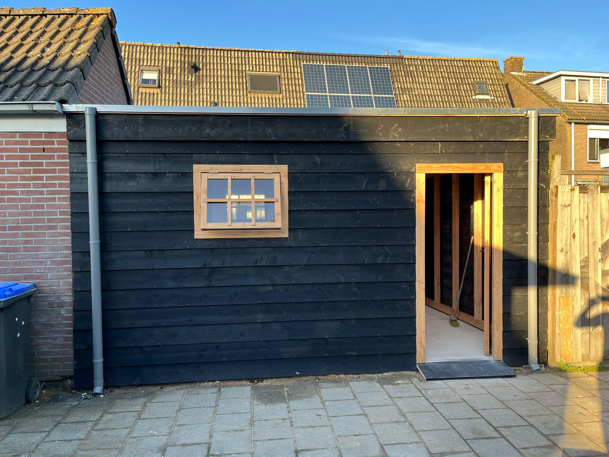 Houten berging: Zwarte berging in de achtertuin, met raampje en deur.